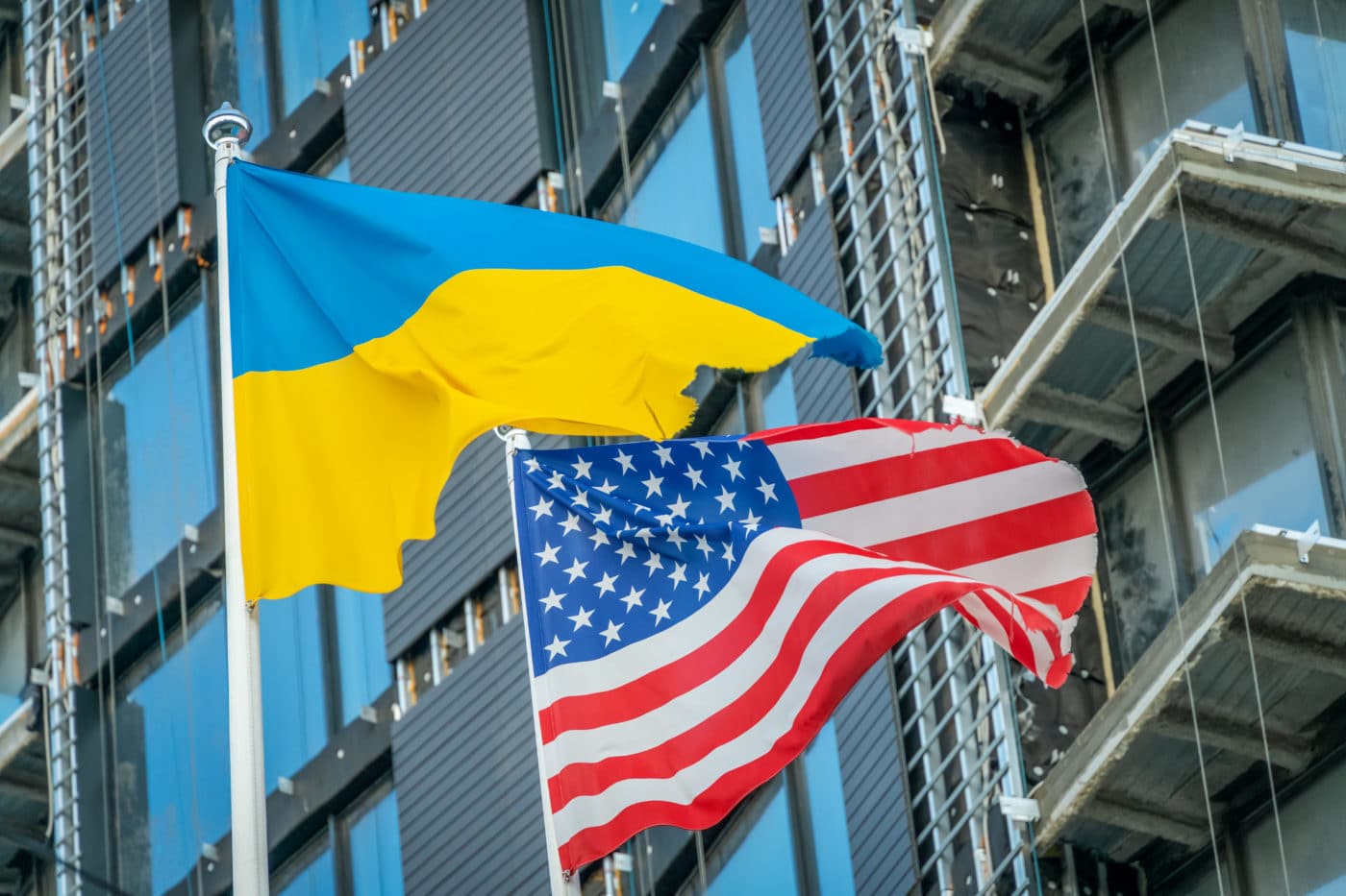 American and Ukrainian flags fly against the blue sky and part of the building. Patriotism.