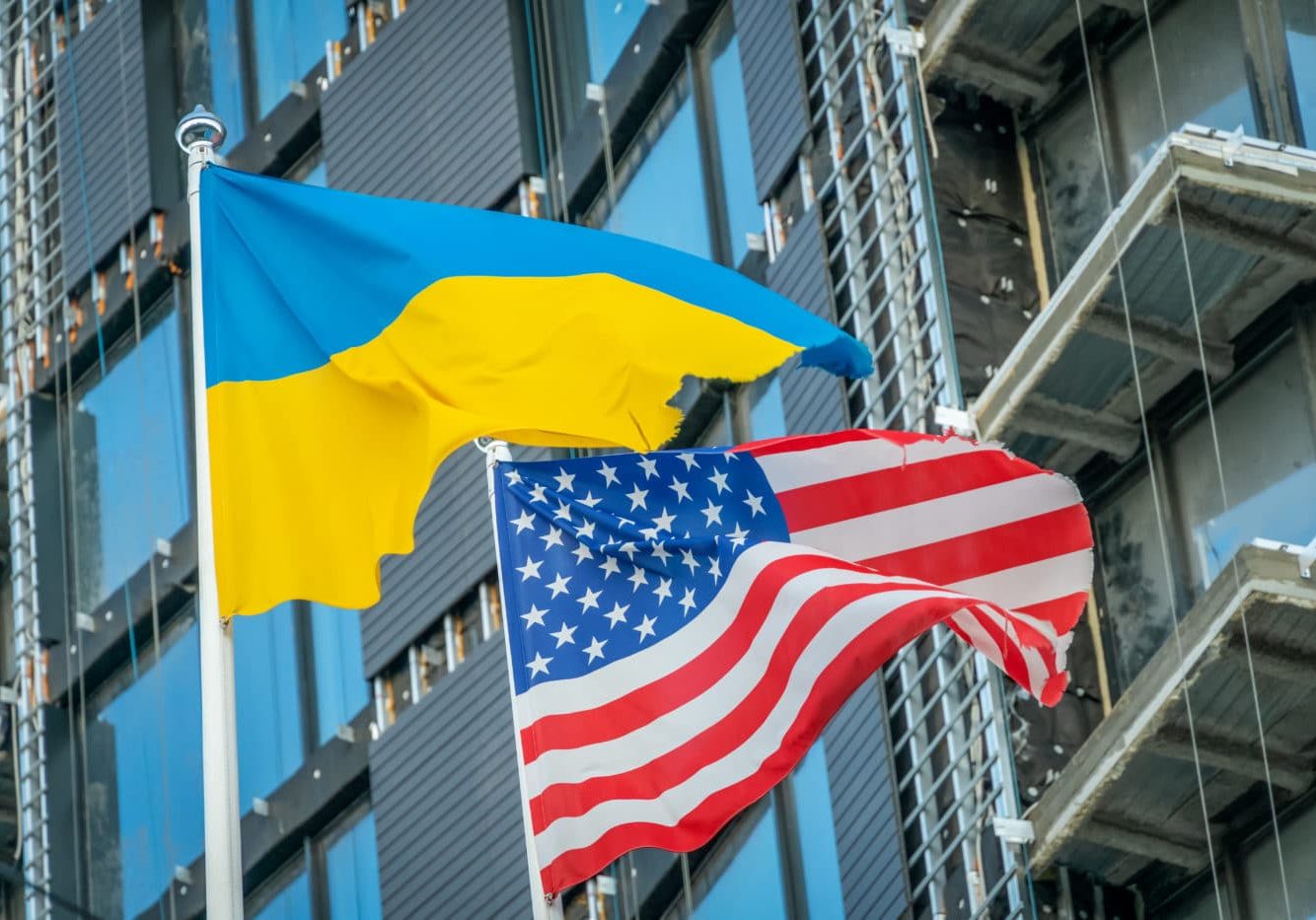 American And Ukrainian Flags Fly Against The Blue Sky And Part Of The Building. Patriotism. American and Ukrainian flags fly against the blue sky and part of the building. Patriotism.